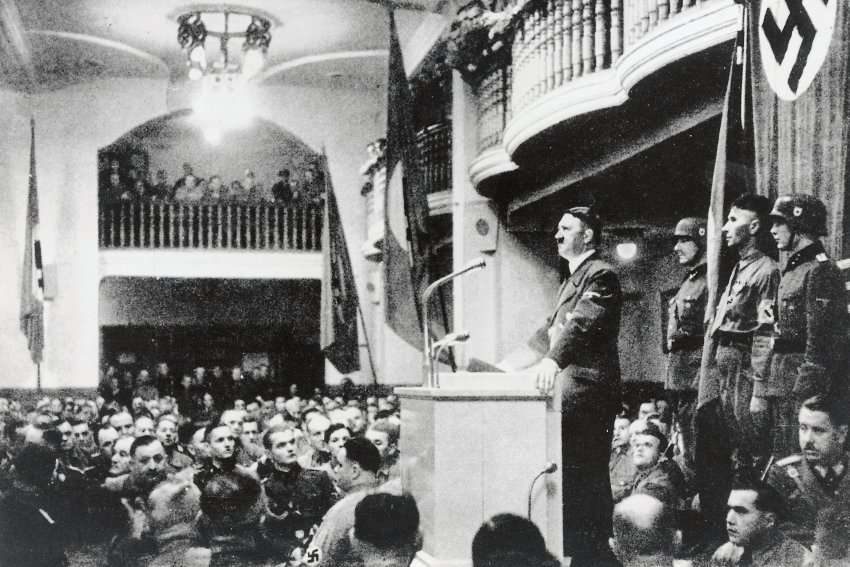 Adolf Hitler spricht am 8. November 1939 im Bürgerbräukeller in München zu den 'alten Kämpfern'. Kaum eine halbe Stunde, nachdem diese Aufnahme gemacht wurde, war die Stelle, wo Hitler gesprochen hatte, durch die Bombe von Johann Georg Elser eine Trümmerstätte.